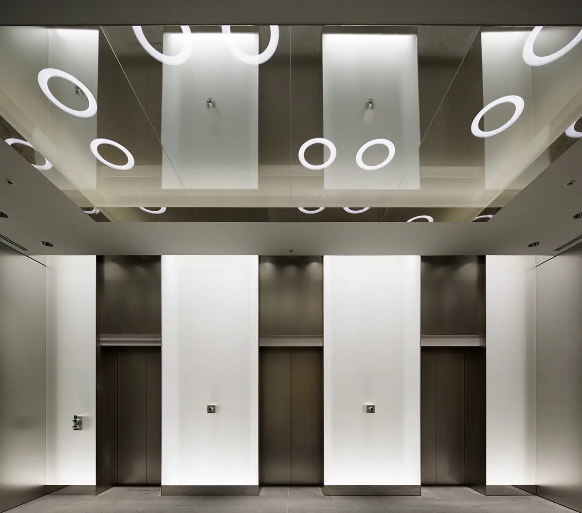 TERASO-Ⅱ：オフィス専用のエレベーターホール。正面の光壁はフロストガラスの内部の上下にLEDシームレスラインを内蔵し、天井はハーフミラーガラスの奥に間接照明とリング上の照明器具を入れることにより、オフィス空間への切替を演出している。